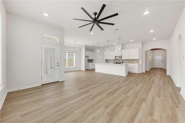 unfurnished living room featuring ceiling fan with notable chandelier and light hardwood / wood-style floors