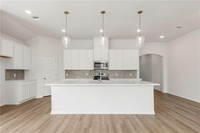 kitchen with stainless steel appliances, white cabinetry, pendant lighting, and a center island with sink