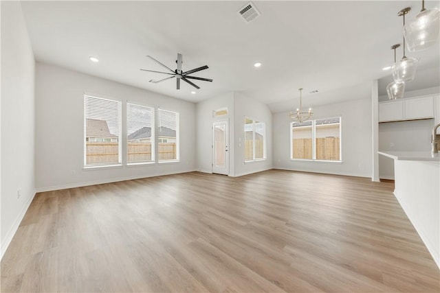 unfurnished living room with ceiling fan with notable chandelier and light wood-type flooring