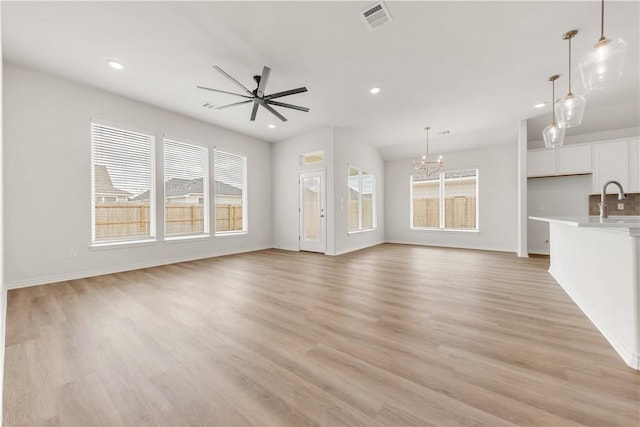 unfurnished living room with sink, ceiling fan with notable chandelier, and light hardwood / wood-style flooring