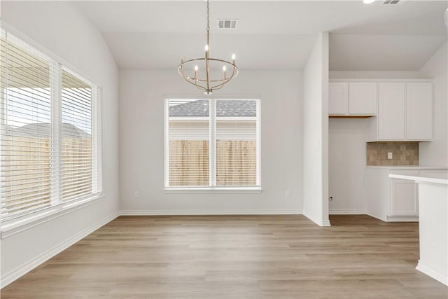 unfurnished dining area with an inviting chandelier, light hardwood / wood-style floors, and lofted ceiling