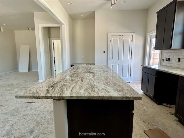 kitchen with tasteful backsplash, light stone countertops, and a kitchen island