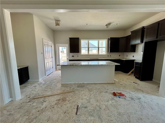 kitchen featuring a kitchen island, light stone counters, dark brown cabinetry, and backsplash