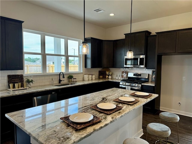 kitchen featuring sink, light stone countertops, decorative light fixtures, a kitchen island, and stainless steel appliances