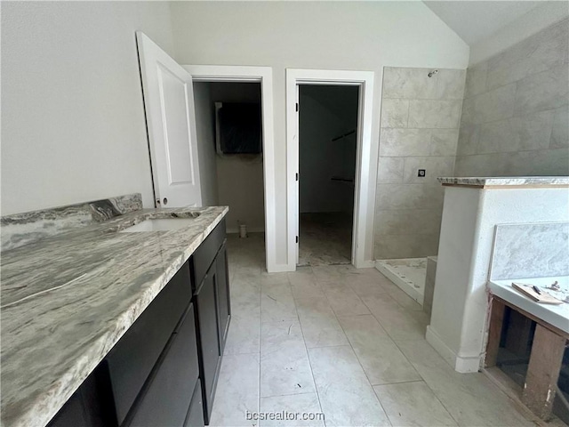 bathroom featuring a tile shower, vanity, and vaulted ceiling