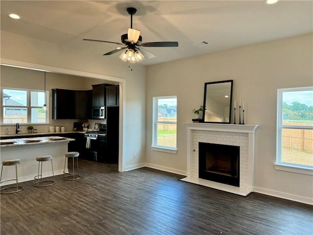 unfurnished living room with ceiling fan, dark hardwood / wood-style flooring, sink, and a brick fireplace