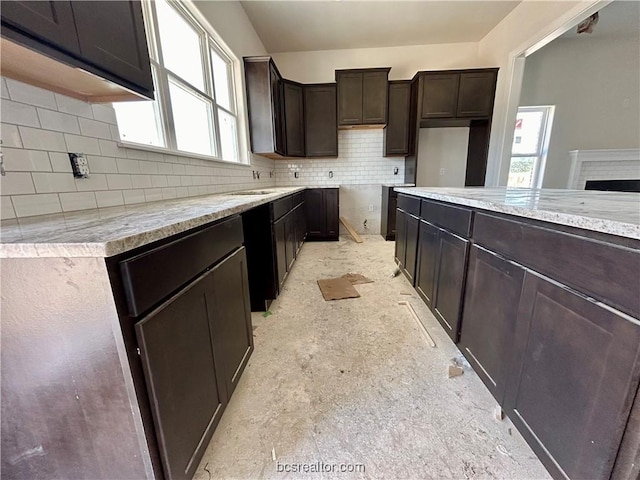 kitchen featuring a center island, tasteful backsplash, dark brown cabinetry, and a brick fireplace