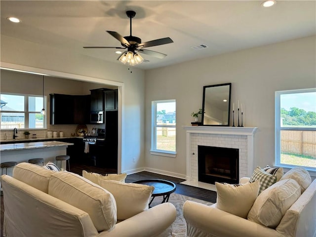 living room featuring ceiling fan, sink, dark hardwood / wood-style floors, and a brick fireplace