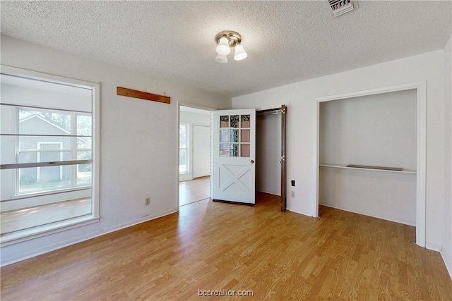 unfurnished bedroom featuring multiple windows, a closet, light hardwood / wood-style floors, and a textured ceiling