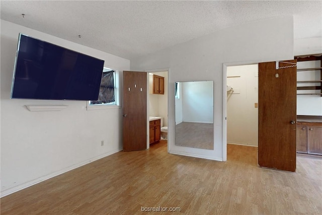 unfurnished bedroom with a textured ceiling, a spacious closet, light hardwood / wood-style flooring, connected bathroom, and a closet