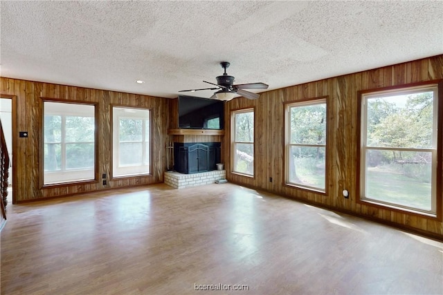 unfurnished living room with a textured ceiling, ceiling fan, light wood-type flooring, and a fireplace