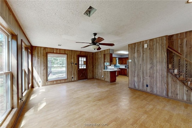 unfurnished living room featuring a textured ceiling, ceiling fan, and wood walls