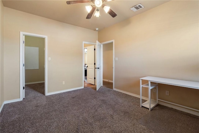 unfurnished bedroom with ceiling fan, dark carpet, and a walk in closet