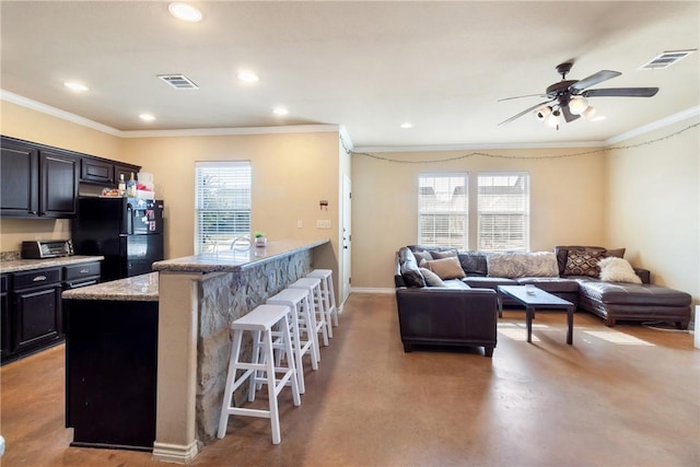 kitchen with a breakfast bar area, crown molding, light stone counters, black refrigerator, and a kitchen island