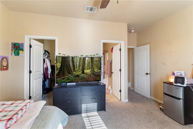 bedroom with stainless steel refrigerator, ceiling fan, light carpet, ensuite bath, and a closet