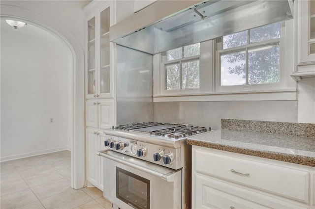 409 N Hutchins St, Bryan, TX 77803 - kitchen featuring high end stainless steel range oven, extractor fan, light tile patterned flooring, light stone countertops, and glass insert cabinets