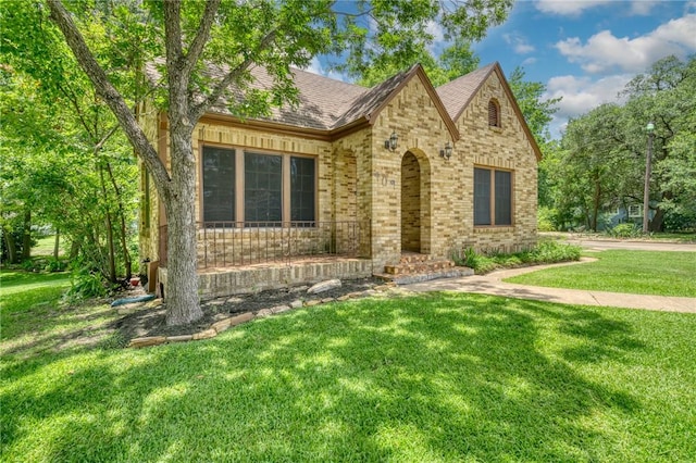 409 N Hutchins St, Bryan, TX 77803 - tudor home featuring a front lawn, brick siding, covered porch, and a shingled roof