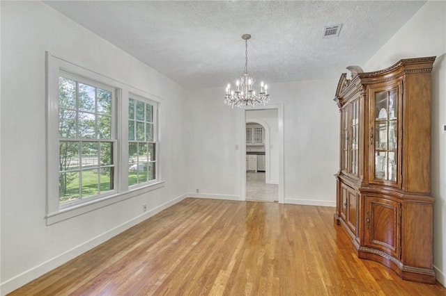 409 N Hutchins St, Bryan, TX 77803 - unfurnished dining area with light wood-style floors, arched walkways, a chandelier, and a textured ceiling