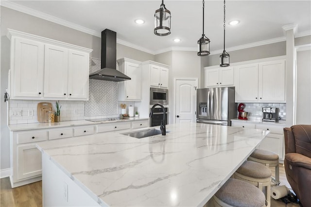 kitchen with appliances with stainless steel finishes, white cabinetry, a center island with sink, decorative light fixtures, and wall chimney exhaust hood