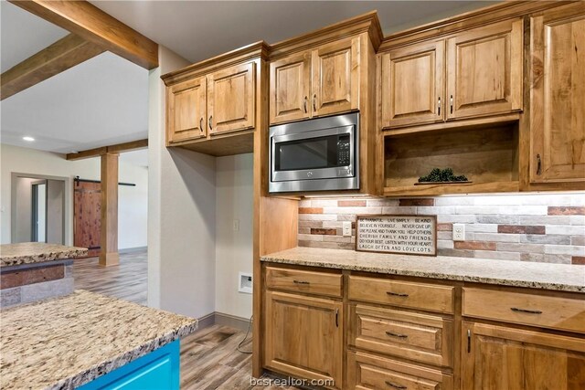 kitchen with a barn door, light stone countertops, stainless steel microwave, and light hardwood / wood-style flooring