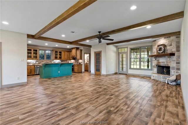 unfurnished living room with beam ceiling, light hardwood / wood-style floors, a stone fireplace, and ceiling fan