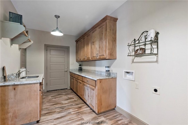 kitchen with decorative light fixtures, light hardwood / wood-style floors, light stone counters, and sink