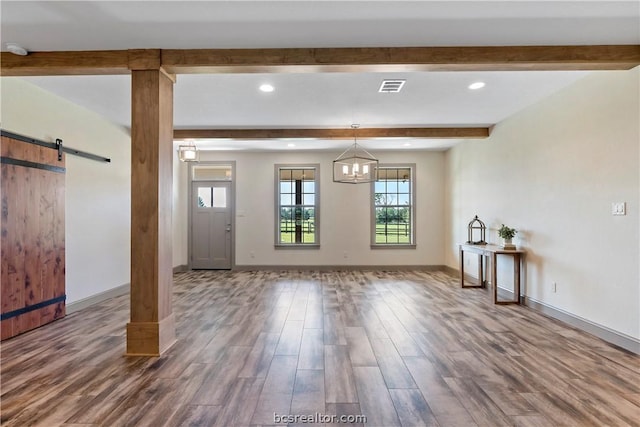 unfurnished living room featuring beam ceiling, a barn door, hardwood / wood-style floors, and a chandelier