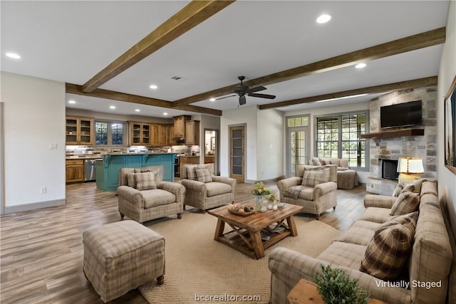 living room featuring a fireplace, beam ceiling, light hardwood / wood-style floors, and ceiling fan