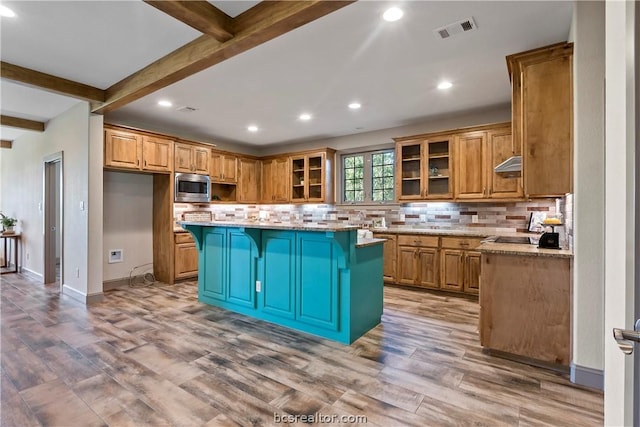 kitchen featuring beam ceiling, light stone countertops, stainless steel microwave, and a kitchen island