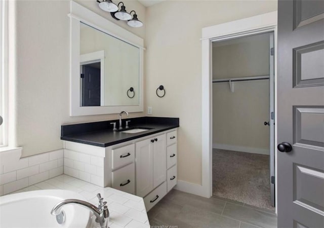 bathroom with tile patterned flooring, vanity, a spacious closet, a tub, and baseboards