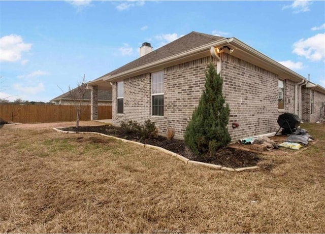view of home's exterior with a chimney, fence, brick siding, a patio, and a yard