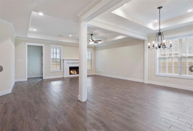 unfurnished living room with ceiling fan with notable chandelier, a raised ceiling, ornamental molding, and dark wood-style floors