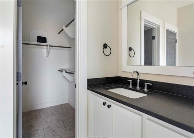 bathroom with baseboards, a walk in closet, and vanity