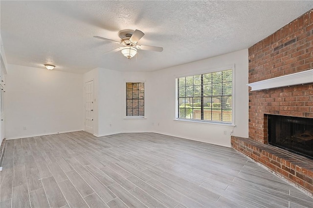 unfurnished living room featuring a brick fireplace, ceiling fan, a textured ceiling, and wood finished floors