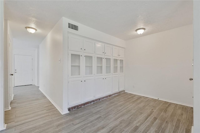 interior space with baseboards, visible vents, light wood-style flooring, and a textured ceiling