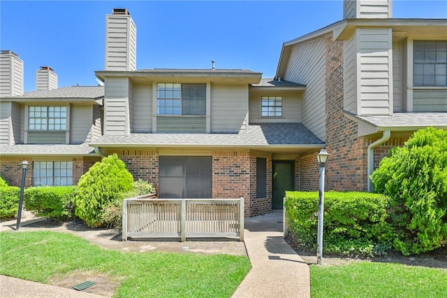 townhome / multi-family property with covered porch, brick siding, a chimney, and roof with shingles