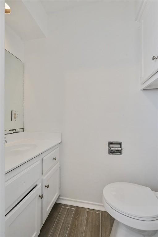 bathroom featuring wood finish floors, toilet, vanity, and baseboards