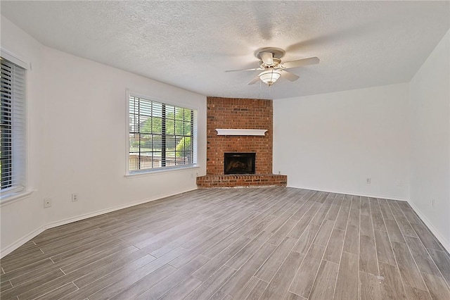 unfurnished living room featuring ceiling fan, a textured ceiling, a fireplace, wood finished floors, and baseboards