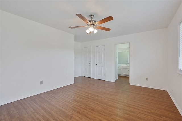 unfurnished bedroom with a ceiling fan, baseboards, wood finished floors, and ensuite bathroom