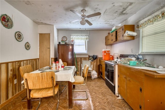 kitchen with electric range oven, wainscoting, freestanding refrigerator, a ceiling fan, and a sink