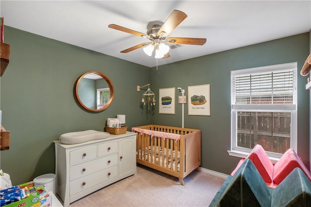 bedroom featuring baseboards, a crib, ceiling fan, and light colored carpet