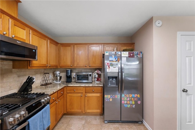kitchen with a toaster, backsplash, appliances with stainless steel finishes, and brown cabinetry