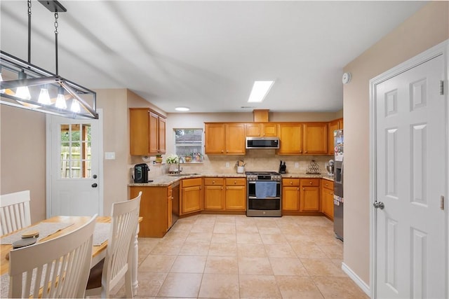 kitchen with a sink, decorative backsplash, light tile patterned floors, light stone counters, and appliances with stainless steel finishes