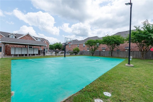 view of basketball court featuring basketball hoop, a lawn, and fence