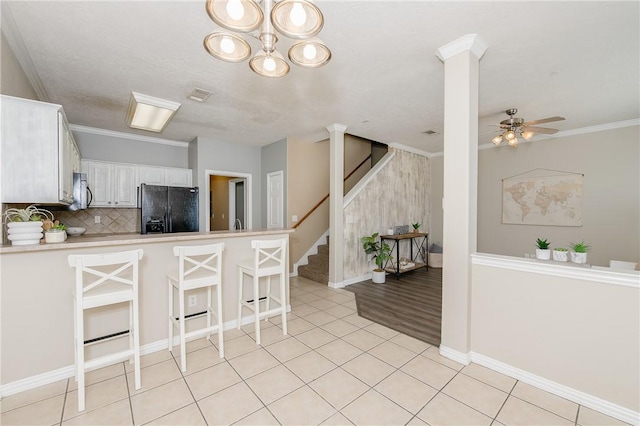 kitchen featuring a peninsula, black fridge, white cabinetry, light countertops, and a breakfast bar area