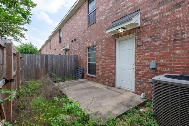 view of side of home with cooling unit, brick siding, and fence