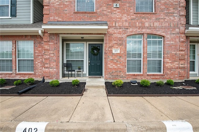 doorway to property with brick siding and roof with shingles