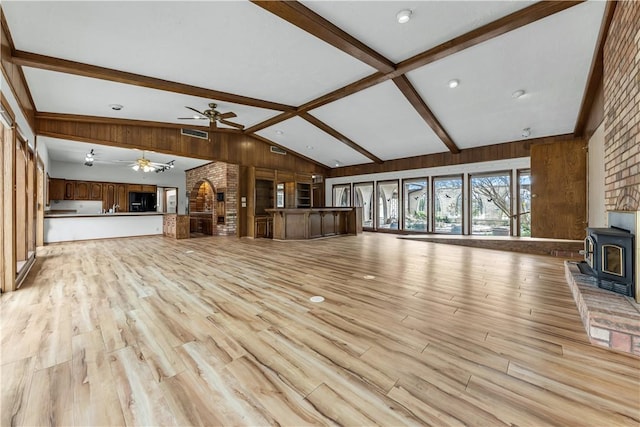 unfurnished living room featuring visible vents, beam ceiling, a wood stove, ceiling fan, and light wood-type flooring