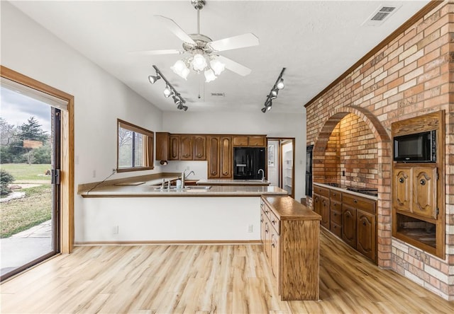 kitchen featuring a sink, light wood-style flooring, black appliances, and a peninsula