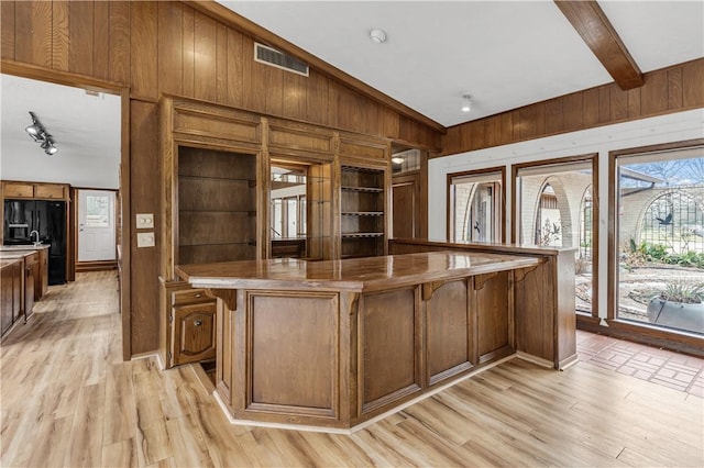 kitchen with light wood-style floors, visible vents, wood walls, and black refrigerator with ice dispenser